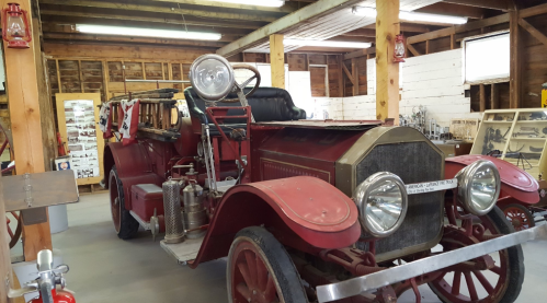 A vintage red fire truck displayed in a rustic museum setting with wooden beams and historical artifacts.