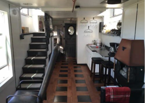 Interior of a cozy, modern tiny home featuring a kitchen, seating area, and staircase, with wooden and black tile flooring.