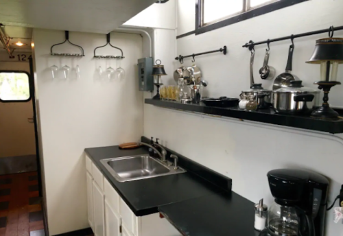 A compact kitchen with a black countertop, sink, hanging glasses, and various cooking utensils and appliances.