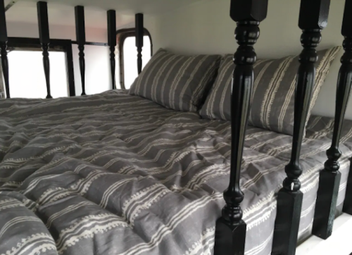 Cozy bed with gray striped bedding and decorative black bedposts in a small, enclosed space.