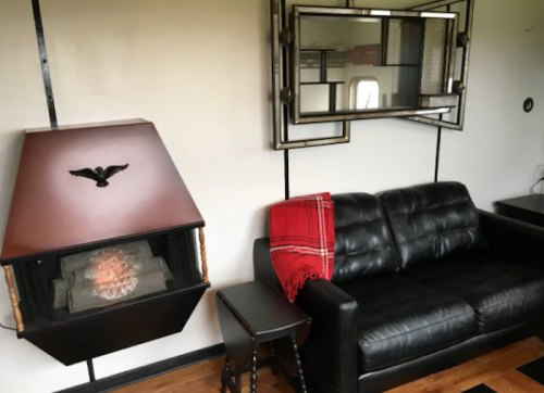 Cozy living space featuring a black leather couch, a plaid throw, a decorative mirror, and a unique fireplace.