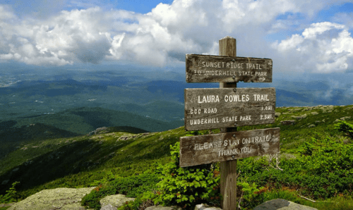 Wooden trail signs at a mountain overlook, with clouds and valleys in the background.