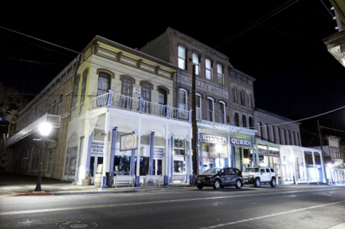 Historic buildings at night, featuring a hotel and shops, with streetlights illuminating the scene.