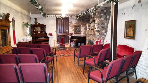 A cozy room with red chairs, a piano, and decorative elements, featuring a stone wall and vintage decor.