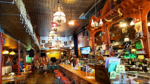 A vintage bar interior with ornate decor, chandeliers, and a long wooden counter, bustling with patrons.