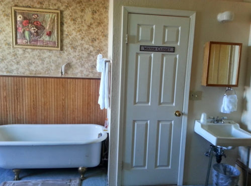 A vintage bathroom featuring a clawfoot tub, a water closet door, a sink, and floral wallpaper.