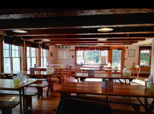 A spacious dining area with wooden tables, large windows, and natural light, featuring pitchers of lemonade on each table.