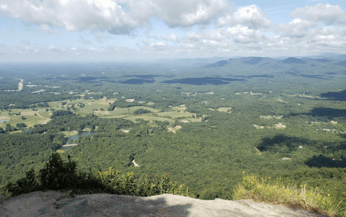 A panoramic view of lush green valleys and distant mountains under a partly cloudy sky.