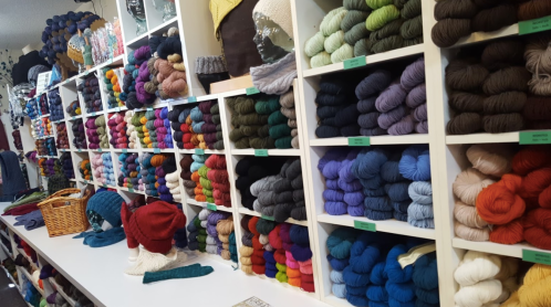 A colorful display of yarn in various shades, neatly organized on shelves in a craft store.