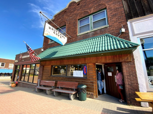 Exterior of Brighton Cafe with a green roof, American flag, and people entering on a sunny day.