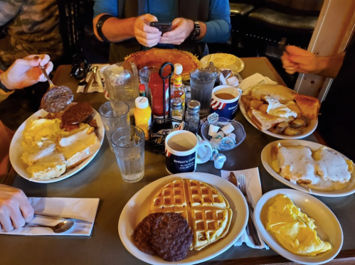 A table filled with a hearty breakfast spread, including eggs, sausage, waffles, pancakes, and drinks.