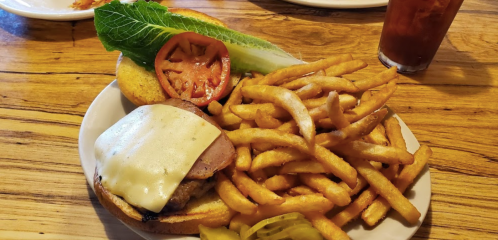 A plate with a cheeseburger topped with lettuce and tomato, served with crispy fries and pickles, alongside a drink.
