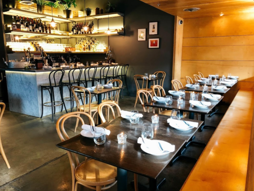 A cozy restaurant interior with wooden tables, chairs, and a well-stocked bar in the background.
