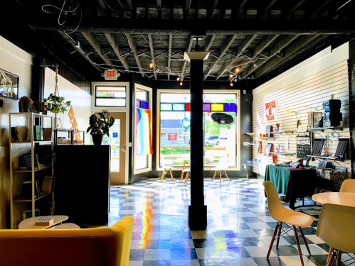 Bright interior of a cozy shop with colorful decor, large windows, and a mix of seating and display areas.