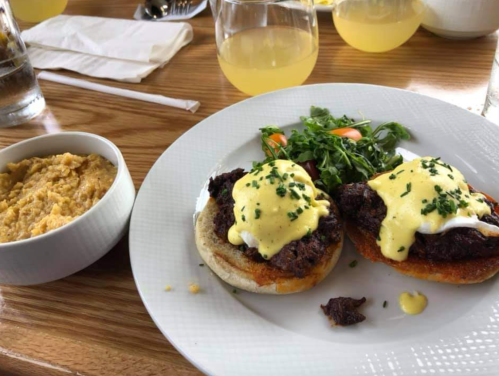A plate featuring two eggs Benedict on toasted buns, garnished with chives, alongside a side of hummus and salad.