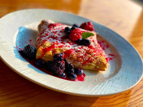 A delicious crepe topped with mixed berries, raspberry sauce, and powdered sugar on a decorative plate.