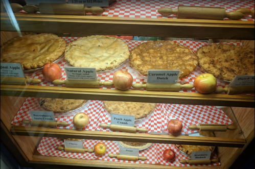 A display case filled with various pies, including apple, caramel apple, and cherry, alongside fresh apples.