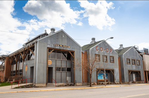 A large, industrial-style building with "CO-OP" signage, set against a blue sky with scattered clouds.