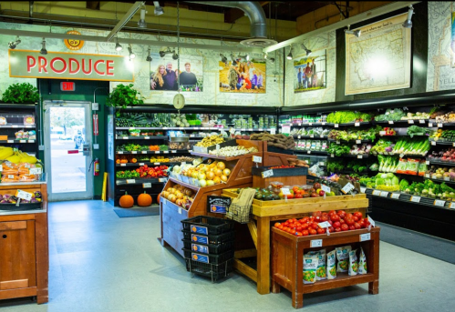 A vibrant produce section in a grocery store, featuring fresh fruits and vegetables, with a welcoming entrance.