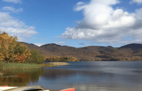 A serene lake surrounded by autumn-colored trees and mountains under a partly cloudy sky.