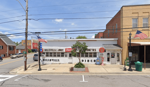 A small diner with a white exterior, American flags, and a sign reading "Hillsville Diner" on a street corner.