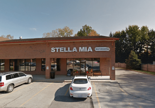 Exterior view of Stella Mia Ristorante, featuring a brick facade and parked cars in front. Trees line the background.