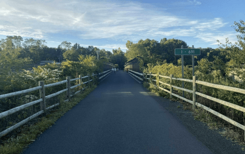 A paved path leads to a bridge surrounded by greenery, with a highway sign for I-691 visible in the background.