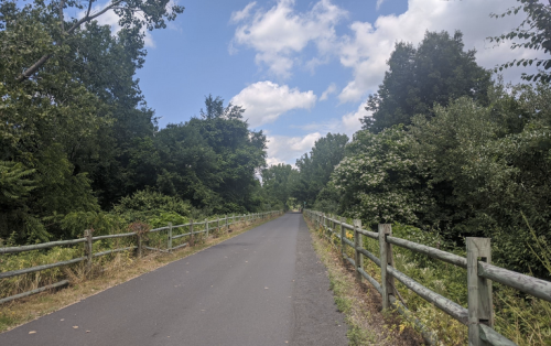 A paved path surrounded by lush greenery and trees under a partly cloudy sky.