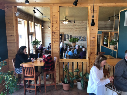 A cozy café interior with wooden decor, plants, and patrons enjoying drinks at tables.