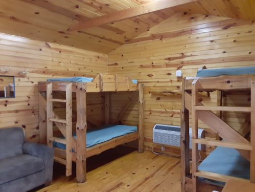 Interior of a wooden cabin with two sets of bunk beds and a couch, featuring a warm, rustic design.