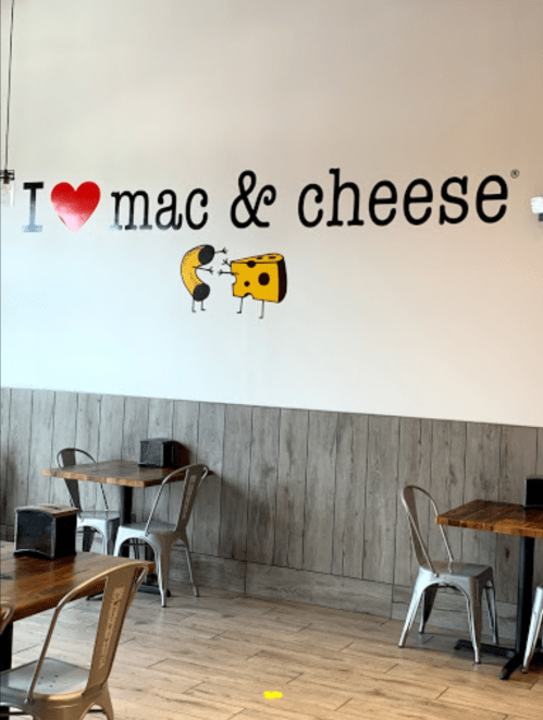 Wall mural in a restaurant featuring "I ❤️ mac & cheese" with cartoon characters of a moon and cheese.