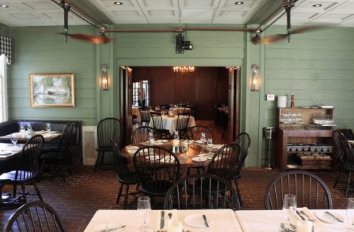 Cozy restaurant interior with green walls, wooden tables, and black chairs, featuring a warm, inviting atmosphere.