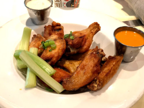A plate of crispy chicken wings with celery sticks and dipping sauces on the side.