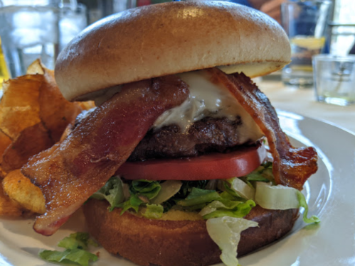 A juicy burger with bacon, lettuce, tomato, and mayo, served with crispy potato chips on the side.