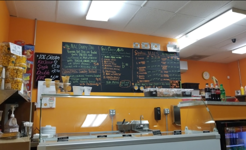 Menu board at a restaurant featuring mac and cheese options, ice cream, and drinks against an orange wall.