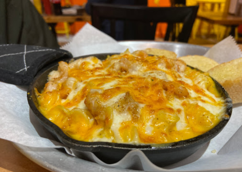 A cast iron skillet filled with cheesy shrimp pasta, served with two slices of bread on the side.