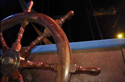 A wooden ship's wheel with a polished finish, set against a dark background.
