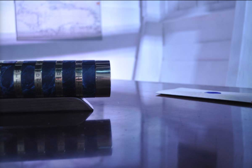 A close-up of a cylindrical object on a desk, with a blue envelope and a map in the background.