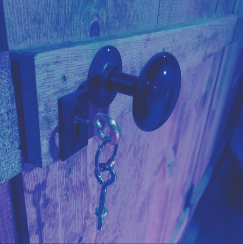 A close-up of a wooden door with a black doorknob and a key inserted in the lock, illuminated in blue light.