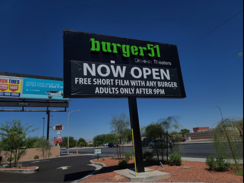 Sign for Burger 51 Drive-In Theaters, stating "Now Open" with details about free short films and adult-only hours.