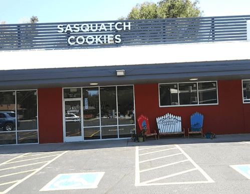 Exterior of Sasquatch Cookies shop with a red and white facade, featuring colorful benches and a sign above the entrance.