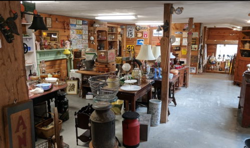 A cozy antique shop filled with various vintage items, furniture, and decor, featuring wooden walls and warm lighting.