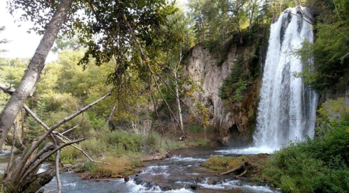 A serene waterfall cascades down rocky cliffs, surrounded by lush greenery and a tranquil stream.