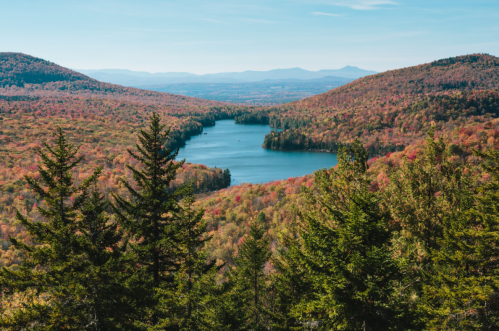 A scenic view of a lake surrounded by colorful autumn foliage and mountains under a clear blue sky.