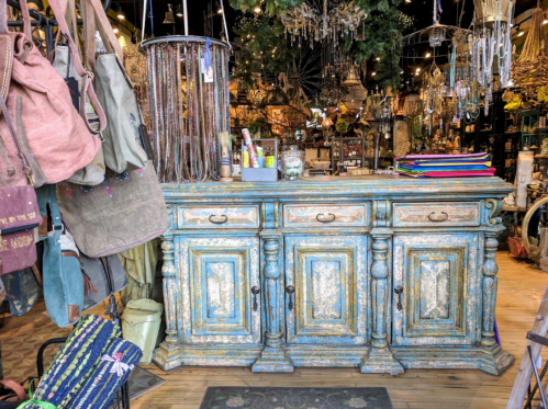 A rustic wooden counter with ornate detailing, surrounded by colorful bags and decorative items in a vibrant shop.