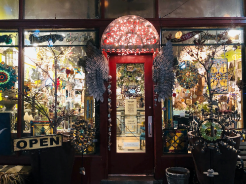 A brightly lit shop entrance with colorful decorations, featuring a red door and signs that say "Open" and "Irresistible Splendor."