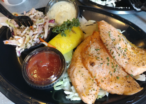 Grilled salmon fillets on a bed of lettuce, served with coleslaw, lemon, and dipping sauces.