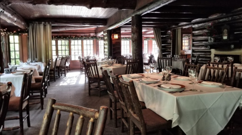 Cozy restaurant interior with wooden beams, tables set for dining, and warm lighting.