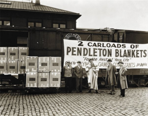 Black and white photo of five people in front of a train, showcasing boxes of Pendleton blankets with a large banner.