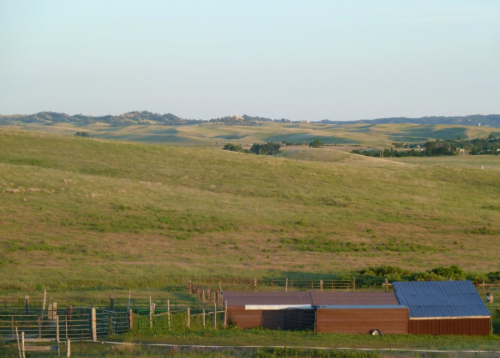 A serene landscape of rolling green hills under a clear sky, with a small barn in the foreground.
